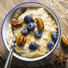 Healthy breakfast: milk porridge from oat bran on skimmed milk with honey, juicy blueberries, pecans on a simple wooden background with a spoon and a jar of honey. Top View.