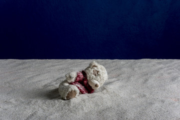Toy bear on white sand and blue background