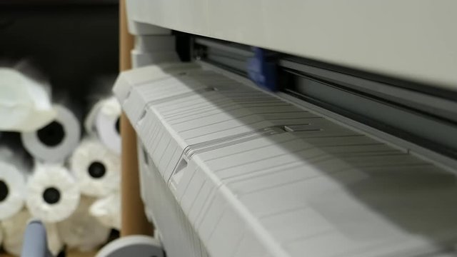 Wide format printer prints and cuts color design draft outline sketch drawing in the printing house. Design office supply equipment in action.