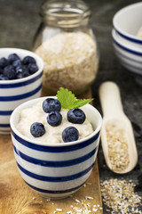 Healthy breakfast: milk porridge from oat bran on skimmed milk with honey, juicy blueberries, pecans on a simple wooden background with a spoon and a jar of honey. Top View.