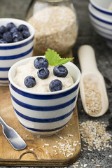Healthy breakfast: milk porridge from oat bran on skimmed milk with honey, juicy blueberries, pecans on a simple wooden background with a spoon and a jar of honey. Top View.