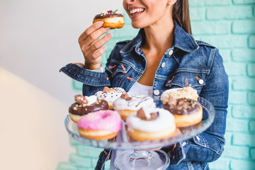 Beautiful young woman enjoying in delicious glazed and decorated donuts. Selective focus on hand...
