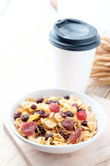 cornflakes and dry berry fruits in a white bowl on a wooden background.