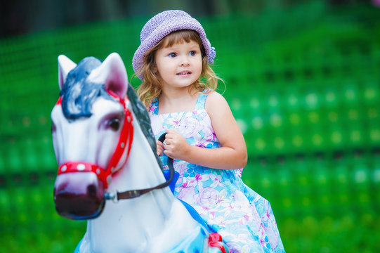 Cute little girl having fun outdoors in the summer park and riding a toy horse