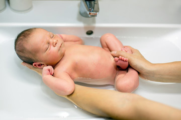 Sweet newborn boy, having his bath in mothers hands