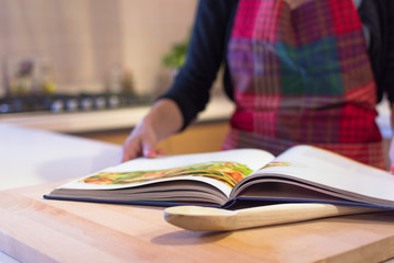 Close-up mid section of a woman, wearing a kitchen apron, reading a recipe book in the kitchen at...