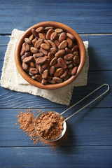 Cocoa beans in bowl and sieve with powder on wooden background