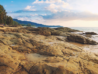 Fototapeta na wymiar Beautiful seascape with sea and rock in Nang Thong Beach, Khao Lak, Thailand. View of bright blue sea with protruding stones in the foreground and crowded beach with bathing and walking people