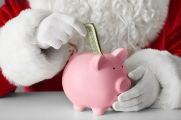 Santa Claus putting money into piggy bank at table
