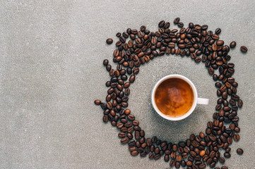 Naklejka premium Black coffee with cream on a gray background surrounded by coffee beans, top view.