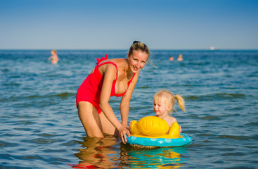 Three-year girl swims in the sea sat on the rubber ring with mother.