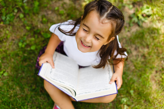 Outdoor portrait of an adorable young little girl reading a book in the garden