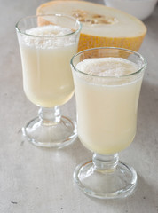 Smoothies of melon in a glass cup on a white wooden table.