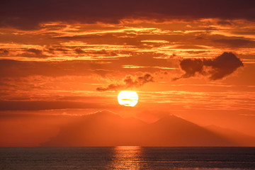 Naklejka premium Beautiful golden orange sunset over the ocean. The sun sets turning the sky yellow, orange & red tones & reflects in the ocean.
