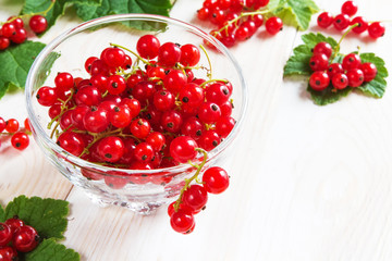 Berries of a red currant in a glass bowl pattern and background of branches of berries and leaves on a light wooden table rural style with copy space, concept of eco nutrition and vegetarianism