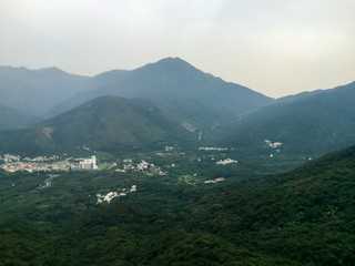 Foggy mountains covered in green forest trees with foggy sky as background and small city building between mountains