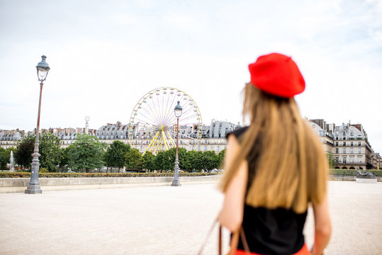 Young woman in red cap and pants walking in Tuileries park with ferry wheel on the background in Paris