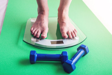 Fototapeta premium Female feet standing on electronic scales, dumbbells. Concept of sports training, slimming and weight loss