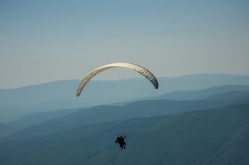 A paragliding tandem flies over a mountain valley on a sunny summer day. Paragliding in the Carpathians in the summer.