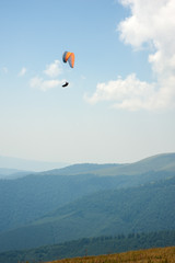 A paragliding tandem flies over a mountain valley on a sunny summer day. Paragliding in the Carpathians in the summer.