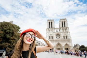 Portrait of a young woman tourist in red cap standing in front of the famous Notre Dame cathedral in Paris