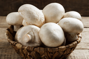 Mushrooms champignons in a wicker basket on a wooden background