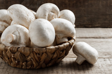 Mushrooms champignons in a wicker basket on a wooden background