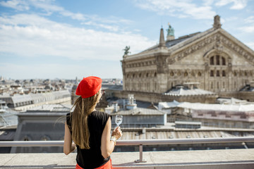 Young woman in red cap relaxing with glass of wine on the terrace with great cityscape view on Paris