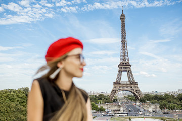 Portrait of a young happy woman in red cap in front of the Eiffel tower in Paris. Woman is out of focus