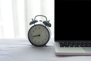 The laptop and alarm clock in the morning on a white bed. copy space. Lifestyle Concept