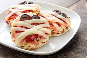 Halloween mummies mini pizzas on wooden table.
