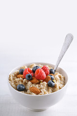 Oatmeal with fresh berry fruits. Oat porridge in a bowl with spoon and blueberries and raspberries.