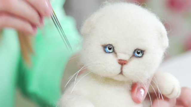 The technique of dry felting from felt: the process of creating cute toys is a white cat. Handicraft, hobby, handicraft. A woman makes toys handmade.