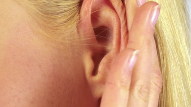 A blonde woman cups her ear to hear better - closeup