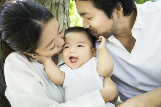 Happy Asian family, kissing a baby boy outdoors