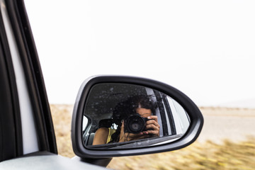 young woman taking a photo from a rear view mirror of a car. Summer. Lifestyle