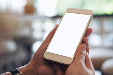 Mockup image of hands holding and using mobile phone with blank white screen in modern cafe with blur bokeh background