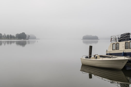 Boat rests on the shore of a lake on a foggy morning