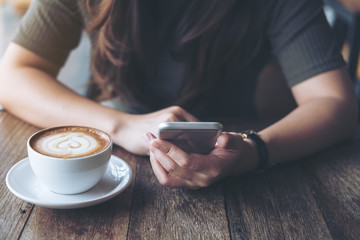 Closeup image of a woman's hands holding , using and pointing at smart phone with latte coffee cup...