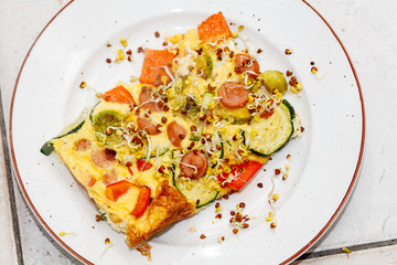 portion of tasty omelette with sausages cut in slices, vegetables on white plate