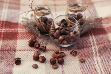 Autumn decorations. Glass jars wrapped in ropes with acorns inside on a brown plaid. Vintage decorations. Selective focus.