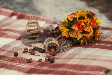 Handmade autumn decorations. Glass jars wrapped in ropes with acorns and chocolate cookies inside on a brown plaid. Bouquet with sunflowers and autumn leaves. Vintage decorations. Selective focus 