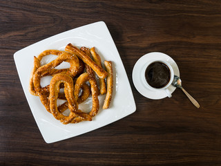 A cup of hot coffee on the wooden table with a plate of Pretzel.