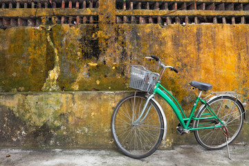 Green vintage bicycle near the old yellow wall.