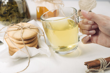 Homemade sugar cookies with honey. Ginger breads with bakery paper tied with a rope on white background. Glass cup of green hot tea. Woman hand