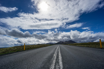 Iceland - Sunshine over straight road between icelandic volcanic mountainous green landscape