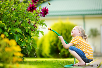 Cute little girl watering flowers in the garden at summer day. © MNStudio