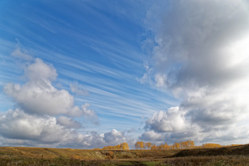 A blue sky with clouds over a autumn landscape with trees in the distance far away in haze