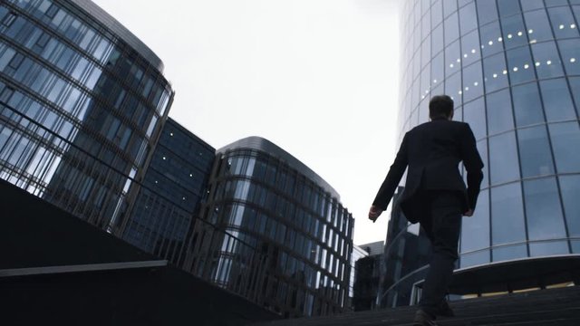Young businessman in suit coming up the stairs. Businessman walking to business center. Lower point shooting. Slow motion - Powered by Adobe