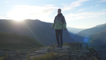 Young man stands high on top of the big mountain at beautiful sunset